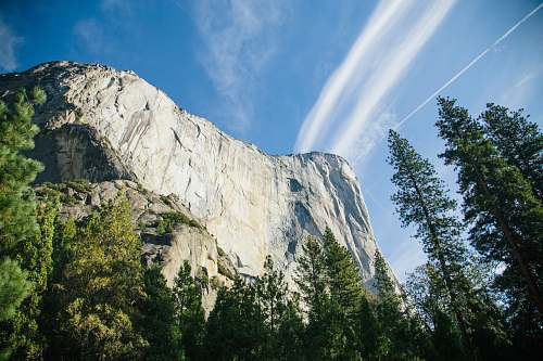 landscape green pine trees beside white rock mountain under white and blue cloudy skies at daytime yosemite valley